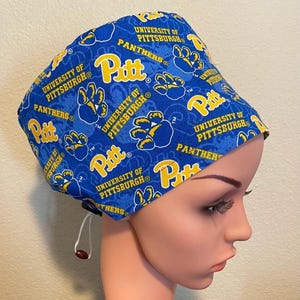 May include: Blue and yellow surgical scrub hat with a repeating pattern of the University of Pittsburgh logo, the word "Pitt", and paw prints.
