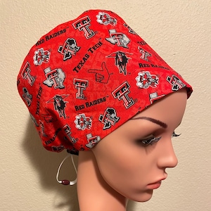 May include: Red and black scrub hat with a Texas Tech Red Raiders logo pattern. The hat has a drawstring and a button.