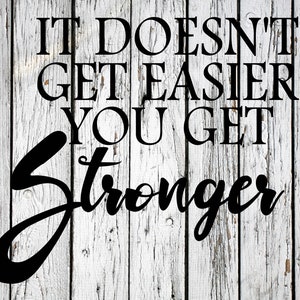 Puede incluir: Texto negro sobre un fondo de madera blanca y desgastada que dice: "IT DOESN'T GET EASIER YOU GET STRONGER." La palabra "Stronger" está escrita en una fuente fluida. La madera tiene un aspecto rústico y desgastado.