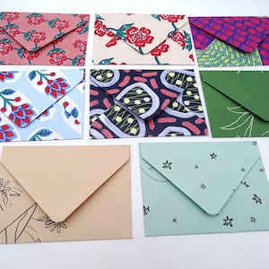May include: A collection of handmade envelopes in various colors and patterns. Designs include floral, geometric, and botanical prints. Some envelopes are solid colors, while others feature star and floral motifs.