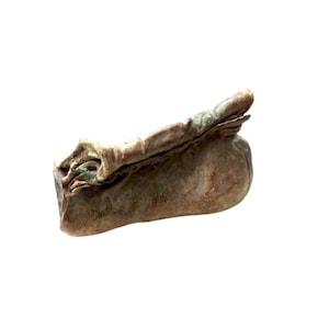 Puede incluir: Una pequeña bolsa de aspecto antiguo con la parte superior doblada. La bolsa es principalmente marrón con toques de verde y rosa, lo que sugiere una apariencia envejecida o desgastada. La textura parece suave y flexible, posiblemente hecha de cuero o material similar.