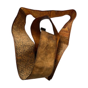 Puede incluir: Un rollo de pergamino antiguo enrollado, con texto manuscrito en tinta marrón oscuro. El rollo es de color marrón claro y tiene una correa de cuero. El texto parece estar escrito en una escritura antigua. El rollo está sobre un fondo blanco.