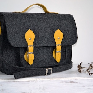 May include: A gray felt satchel bag with yellow leather accents and buckles. The bag has a long shoulder strap and a top handle.