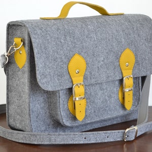 May include: A gray felt satchel bag with yellow leather accents and buckles. The bag has a long adjustable strap and a top handle.