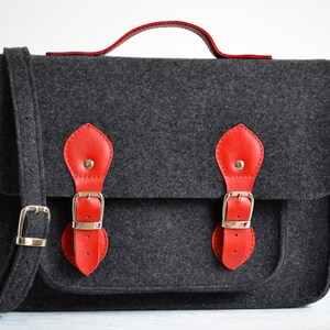 May include: A gray felt satchel bag with red leather accents and silver buckles. The bag has a top handle and a long adjustable shoulder strap.