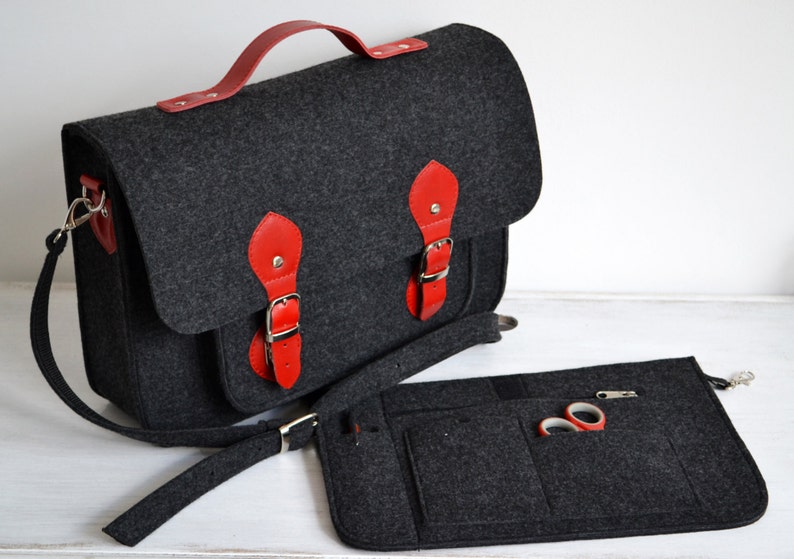 May include: A gray felt satchel bag with red leather accents and a matching felt pouch. The bag has a top handle and a long adjustable shoulder strap. The pouch has multiple pockets and a zipper closure.
