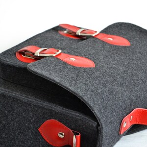 May include: A gray felt messenger bag with red leather accents and silver buckles. The bag has a top flap with a buckle closure and a red leather handle.