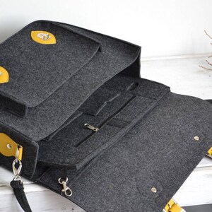 May include: A gray felt laptop bag with yellow leather accents and a zippered pocket. The bag has a long strap and a top handle.