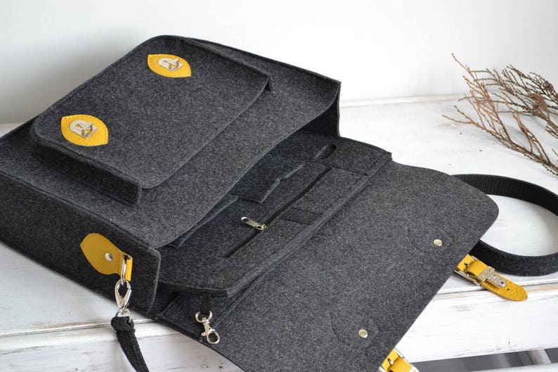 May include: A gray felt laptop bag with yellow leather accents and a zippered pocket. The bag has a long strap and a top handle.
