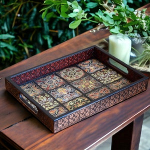 Puede incluir: Una bandeja rectangular de madera con un borde de color cobre y un diseño estampado de azulejos coloridos. La bandeja tiene dos asas a los lados.