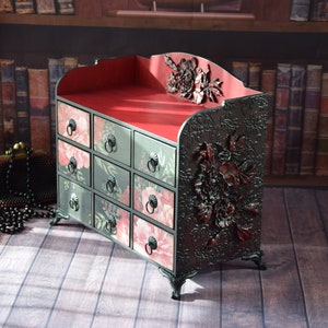 May include: A black wooden chest with 12 drawers, each with a floral design. The chest has a red velvet lining and ornate floral carvings on the sides.