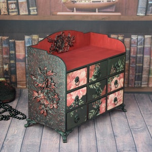 May include: A black wooden drawer organizer with a red top and floral patterned drawers. The organizer has a floral design on the front and is decorated with a 3D floral accent.