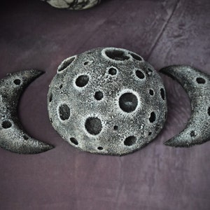 May include: Three grey, textured, crescent moon shapes with craters. The centre moon is full and the two outer moons are half moons.