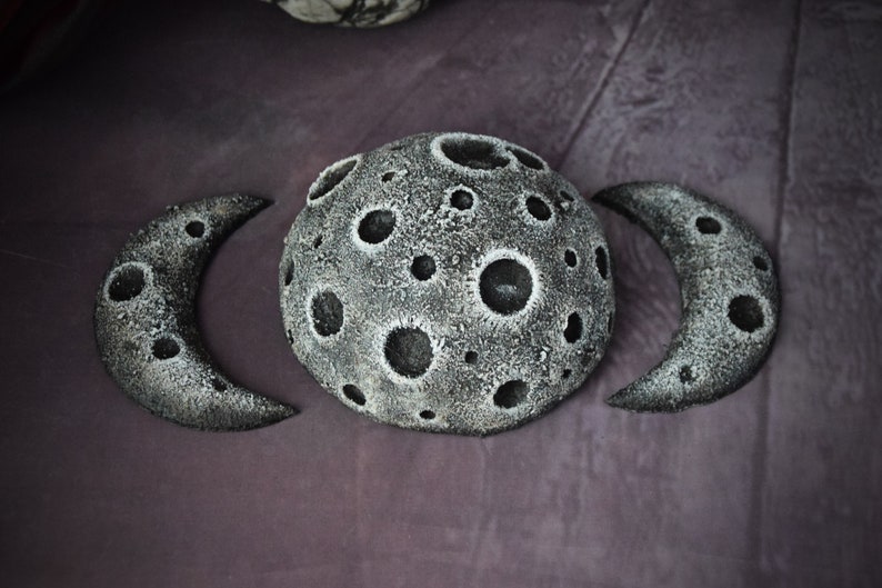 May include: Three grey, textured, crescent moon shapes with craters. The centre moon is full and the two outer moons are half moons.