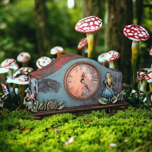 May include: A vintage-style clock with a white face and black Roman numerals, surrounded by mushrooms and a whimsical Alice in Wonderland character. The clock is decorated with a floral design and has a wooden base.