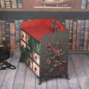 May include: A small, multi-drawered wooden box with a red top and floral carvings. The box is decorated with a floral pattern and has a dark brown finish.