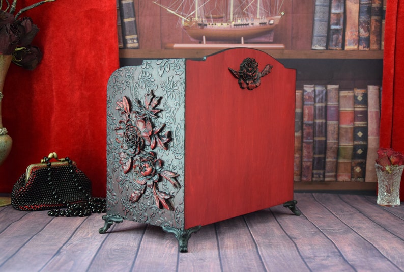 May include: A red wooden magazine rack with carved floral details and black metal feet. The rack is decorated with a floral design and has a red finish.