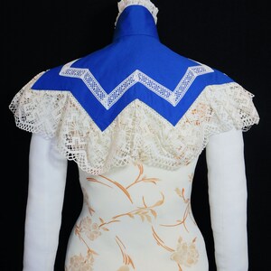 May include: A white lace collar with a blue fabric insert. The collar has a scalloped edge and a zig-zag pattern.
