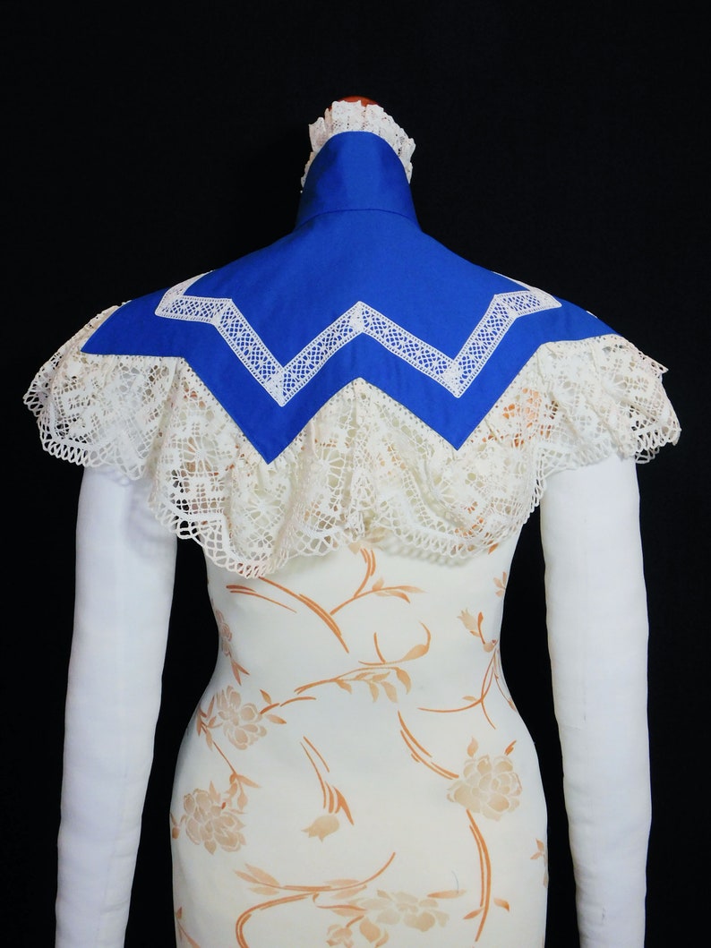 May include: A white lace collar with a blue fabric insert. The collar has a scalloped edge and a zig-zag pattern.