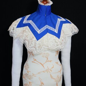 May include: A white lace collar with a blue fabric insert. The collar is on a white dress form with long white sleeves.