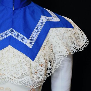 May include: A blue collar with white lace trim. The collar is made of a thick fabric and has a pointed shape. The lace trim is delicate and intricate.