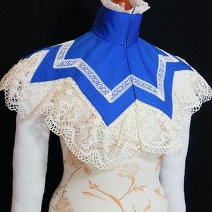 May include: A blue lace collar with a white lace trim. The collar is on a white dress form with a floral pattern.