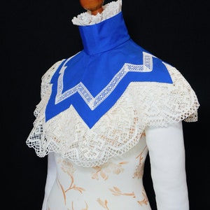 May include: A white lace collar with a blue satin lining. The collar has a scalloped edge and a zig-zag pattern.