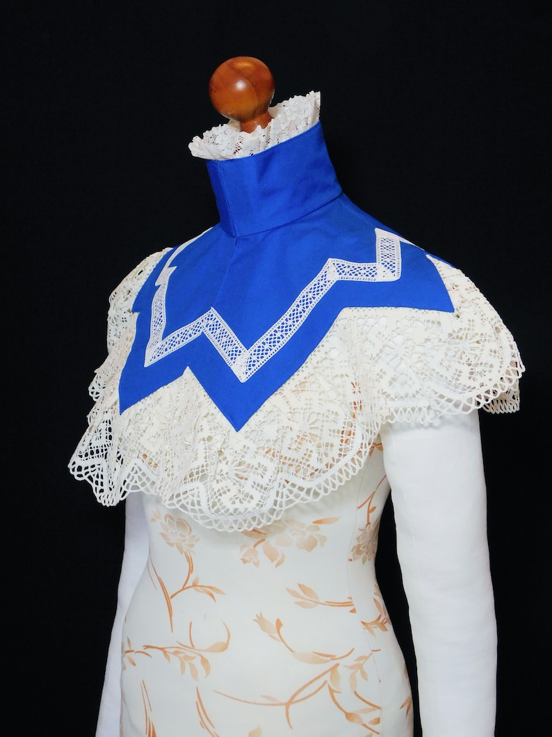 May include: A white lace collar with a blue satin lining. The collar has a scalloped edge and a zig-zag pattern.