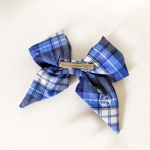 May include: A blue and white plaid bow with a silver clip. The bow has a small embroidered letter "S" on one side.