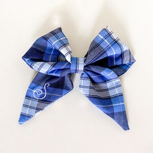May include: A blue and white plaid bow with a white embroidered letter "S" in the center.