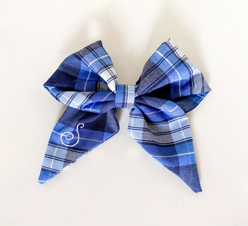 May include: A blue and white plaid bow with a white embroidered letter "S" in the center.