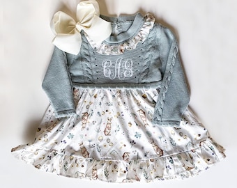 May include: A light blue knitted dress with a white ruffle collar and a white floral print skirt. The dress has a cable knit pattern and is monogrammed with the letters "CGS".