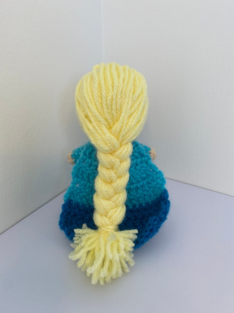 May include: A crocheted doll with a blue and teal dress and long yellow braided hair.