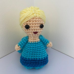 May include: A crocheted doll with blonde hair, a blue dress, and black eyes.