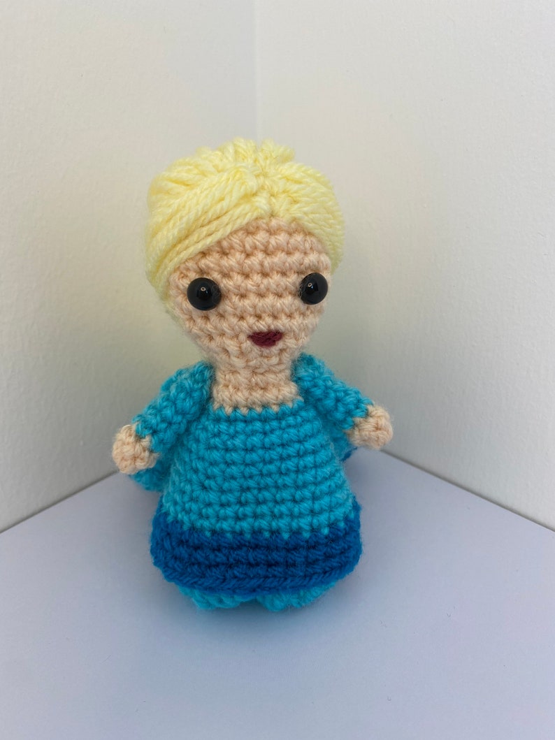May include: A crocheted doll with blonde hair, a blue dress, and black eyes.