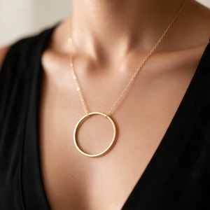 May include: A gold-toned necklace featuring a thin, circular pendant suspended from a delicate, matching gold-toned chain. The pendant is a simple, smooth, open ring shape that hangs centrally against the chest, creating a clean and balanced look.