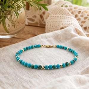 May include: A beaded bracelet featuring alternating faceted turquoise-coloured stones and small, polished gold-toned metal spheres. The circular jewellery piece is finished with a gold-toned metal lobster claw clasp closure at the back.