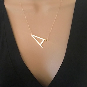 May include: A gold necklace with a simple, geometric letter 'A' pendant.