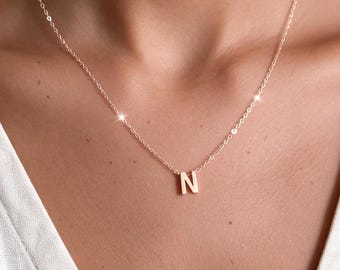 May include: A delicate rose gold-toned necklace featuring a small, polished letter N pendant suspended from a thin, matching cable chain. The metal has a warm, metallic sheen, and the pendant is centred on the chain, resting against the skin.
