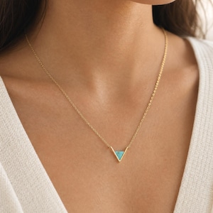 May include: A gold-toned necklace featuring a delicate chain and a V-shaped pendant. The pendant is inlaid with a small, triangular piece of bright turquoise stone, creating a clean geometric design that rests against the collarbone area.