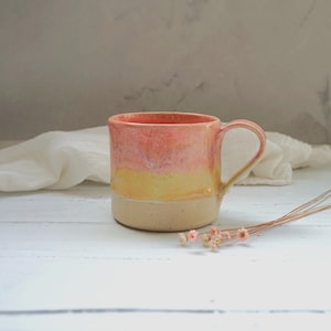 May include: A white ceramic mug with a black handle and the text "But First, Coffee" in a black, handwritten-style font. The mug is on a white surface.