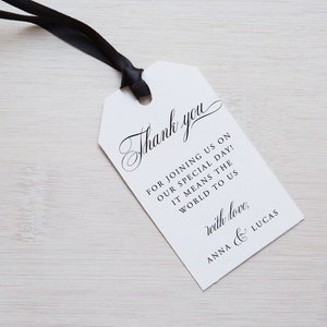 May include: White wedding favor tag with black text that reads "Thank you for joining us on our special day! It means the world to us with love, Anna & Lucas".