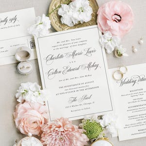 May include: Elegant wedding invitation suite featuring a main invitation, reply card, and details card. The design includes delicate script, floral accents, and a ring box with a diamond ring. Soft pink and white flowers surround the stationery.