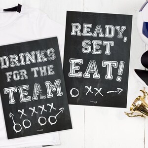 Puede incluir: Dos letreros negros de pizarra con texto blanco. El primer letrero dice "Drinks for the Team" con un diagrama de jugada de fútbol. El segundo letrero dice "Ready, Set, Eat!" con un diagrama de jugada de fútbol.