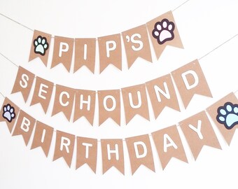 May include: A brown paper banner with white letters that reads "PIP'S SCHOUNBD BIRTHDAY". The banner is decorated with paw prints in various colors.