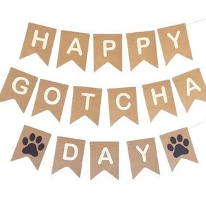 May include: A brown paper banner with the text "Happy Gotcha Day" in white letters. The banner has paw prints in black on the ends.