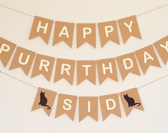 May include: A brown paper banner with the words "Happy Purrthday Sid" in white letters. The banner has two black cat silhouettes on either end.
