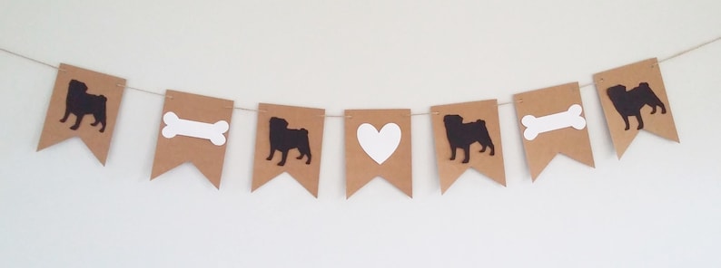 May include: A brown and white banner with alternating images of a pug, a bone, a heart, and a pug. The banner is strung together with white twine.