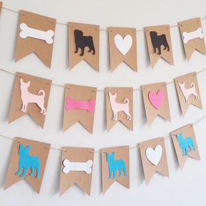 May include: A brown paper banner with cutouts of dogs, hearts, and bones. The dogs are a black pug, a pink chihuahua, and a blue french bulldog. The hearts are white and pink. The bones are white and pink.