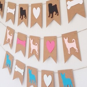 May include: A brown paper banner with cutouts of dogs, hearts, and bones. The dogs are in black, pink, and blue silhouettes. The hearts are white and pink. The bones are white.